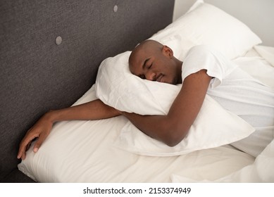 Handsome Young Black Man Sleeping Alone, Hugging Soft Pillow, African American Guy Lying Asleep In Comfortable Cozy Bed Enjoying Peaceful Healthy Sleep
