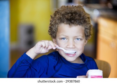 Handsome young boy with blue eyes eating yogurt