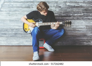 Handsome Young Boy With Electric Guitar Sitting On Amplifier In Wooden Room. Music, Concert Rehearsal Concept