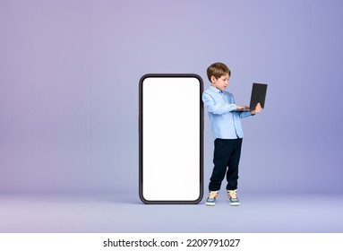 Handsome Young Boy Wearing Formal Wear Is Standing Holding Laptop Near Large Empty White Mockup Smartphone Case In Background. Purple Wall. Concept Of Gadgets, Learning, Studying, Progressive Kids