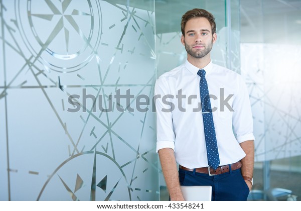 Handsome young business executive looking\
confidently at the camera while leaning against patterned glass\
office dividers in a modern\
workplace\
