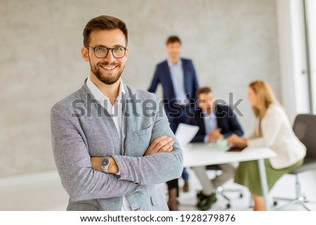 Handsome young business man standing confident in the office in front of his team