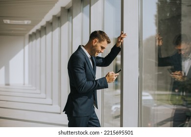 Handsome Young Business Man Using Mobile Phone In The Modern Office Hallway