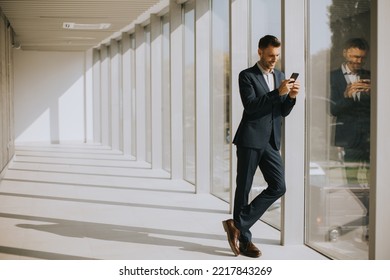 Handsome Young Business Man Using Mobile Phone In The Modern Office Hallway