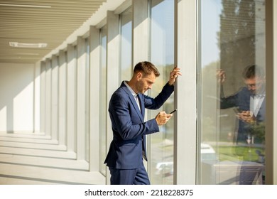 Handsome Young Business Man Using Mobile Phone In The Modern Office Hallway