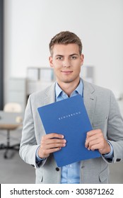Handsome Young Businessman Inside the Office, Holding a Blue Document Folder and Smiling at the Camera.