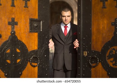 Handsome Young Businessman Opening The Door. Wooden Arched Double Doors. Detail Of An Old Castle Door.