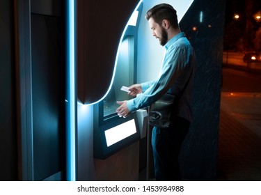 Handsome young businessman putting credit card in ATM at night 