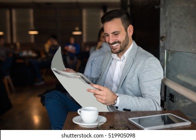 Handsome young businessman reading newspaper at a sidewalk cafe. Morning routine. - Powered by Shutterstock