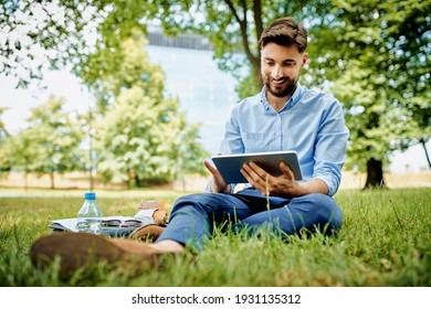 Handsome young businessman sitting outdoors in the park and using tablet - Powered by Shutterstock