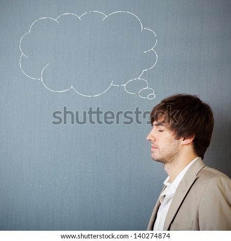 Handsome young businessman with thought bubble drawn on blue wall