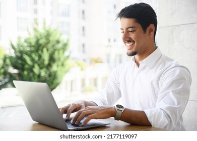 Handsome young businessman is using laptop outdoors. Hispanic guy office employee is typing on the keyboard, replying to emails, multiracial male freelancer in smart casual wear working remotely - Shutterstock ID 2177119097