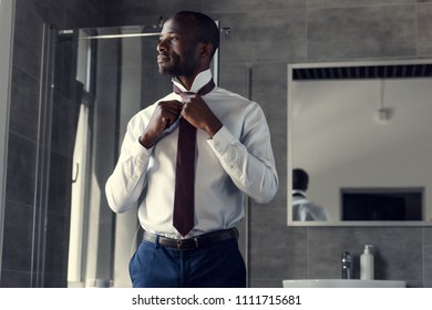 handsome young businessman in white shirt putting on his tie at bathroom - Powered by Shutterstock