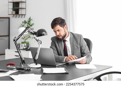 Handsome young businessman working with documents and laptop at table in office - Shutterstock ID 2254377575