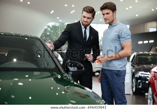 Handsome young car salesman showing a new car\
to the customer at the\
dealership