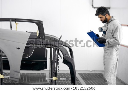 handsome young caucasian auto mechanic in uniform is making notes while examining car in auto service, check it before repair. diagnostics concept