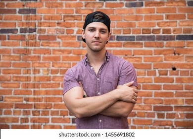 Handsome Young Caucasian Man with Backwards Hat Smiling for Portraits in Front of Textured Brick Wall Outside - Powered by Shutterstock