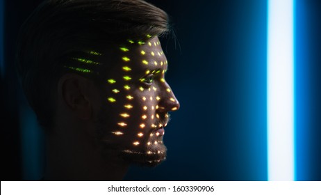 Handsome Young Caucasian Man is Identified by Biometric Facial Recognition Scanning Process. Futuristic Concept: Projector Identifies Individual by Illuminating Face by Colorful Dots and Laser
