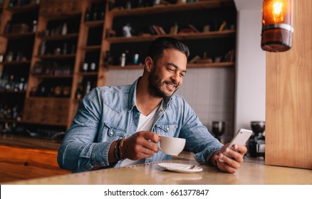 Handsome young caucasian man sitting at cafe using mobile phone and having coffee. Caucasian male with cup of coffee and reading text message on his smart phone. - Powered by Shutterstock