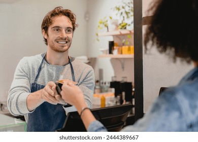 Handsome young caucasian waiter servicing the customer with swiping machine in a cafe. Cashless contactless payment with credit debit card. E-banking e-commerce concept - Powered by Shutterstock