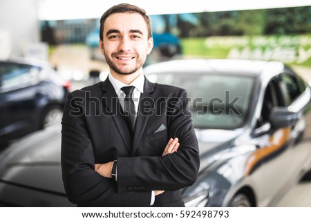 Handsome young classic car salesman standing at the dealership in front of new car