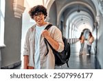 Handsome young confident college student. Smiling male student with backpack and books walking on campus indoors. Young man ready for classes or studying. Confident and happy college student.       