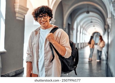 Handsome young confident college student. Smiling male student with backpack and books walking on campus indoors. Young man ready for classes or studying. Confident and happy college student.       