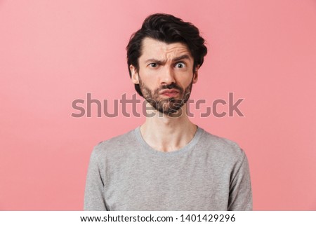 Handsome young confused bearded brunette man wearing sweater standing isolated over pink background