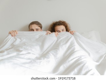 Handsome young couple slept together, covered their faces with a blanket and looked at  camera.