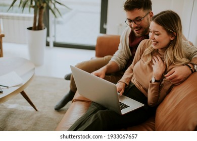 Handsome young couple using laptop together while sitting on sofa at home - Shutterstock ID 1933067657