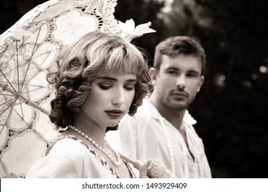 Handsome young couple in vintage clothing with beautiful woman looking down as handsome man watches her, lovingly
