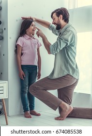 Handsome young dad is measuring his cute little daughter's height on the wall in childs room