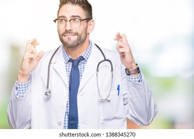 Handsome young doctor man over isolated background smiling crossing fingers with hope and eyes closed. Luck and superstitious concept.