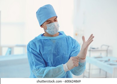 Handsome young doctor putting on rubber gloves in clinic