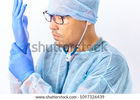 Handsome young doctor with a stethoscope around the neck putting on rubber gloves in hospital or clinic