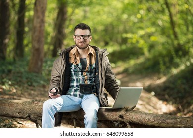 Handsome Young Environmentalist Is Using Laptop, Mobile Phone And Camera In The Woods