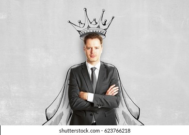 Handsome Young European Man With Drawn Crown And Cape On Concrete Wall Background. Leadership Concept