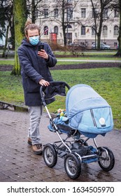 Handsome Young European Man In Winter Clothes On The Street With A Medical Face Mask On And Baby Carriage. 35-year-old Male In A Respirator To Protect Against Infection With  Coronavirus