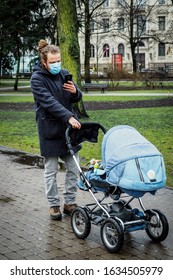 Handsome Young European Man In Winter Clothes On The Street With A Medical Face Mask On And Baby Carriage. 35-year-old Male In A Respirator To Protect Against Infection With  Coronavirus