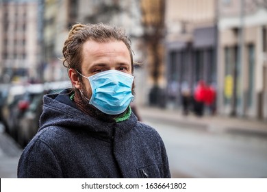 Handsome young European man in winter clothes on the street with a medical face mask on. Closeup of a 35-year-old male in a respirator to protect against infection with influenza virus or coronavirus