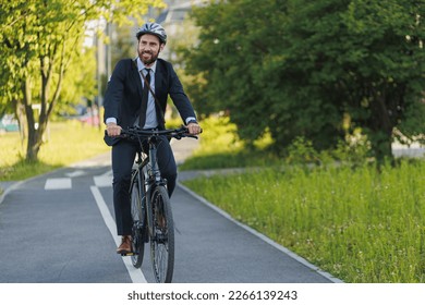 Handsome young executive in elegant suit riding on bike lane in sunny day. Front view of busy businessman wearing protective helmet getting to work by bicycle on bike lane. Concept of bike commute.