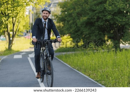 Handsome young executive in elegant suit riding on bike lane in sunny day. Front view of busy businessman wearing protective helmet getting to work by bicycle on bike lane. Concept of bike commute.