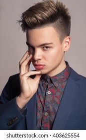 Handsome Young Fashion Model With Highlighted Undercut Haircut Posing In Blue Suit In Studio Looking With Passion At Camera With Finger On His Face.