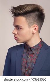 Handsome Young Fashion Model With Highlighted Undercut Haircut Posing In Blue Suit In Studio Side Looking.