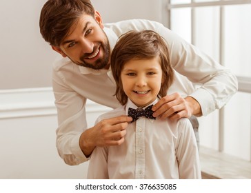 Handsome young father adjusting his cute little son's bow tie. Both white classical shirts looking in camera and smiling - Powered by Shutterstock