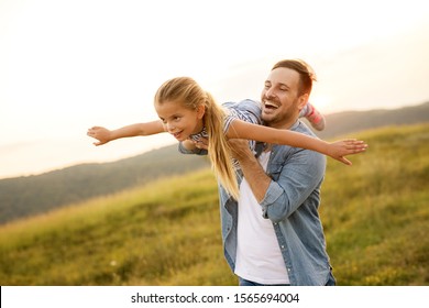 Schöner junger Vater in grüner, sonniger Sommernatur, der seine süße kleine Tochter in den Armen hält.