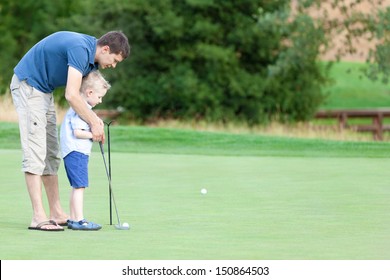 handsome young father teaching his cute son to play golf