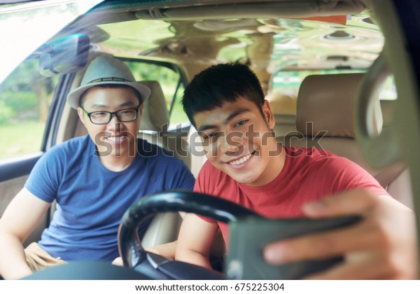 Handsome\
young friends taking picture of themselves on smartphone while\
sitting in car ready for unforgettable road\
trip