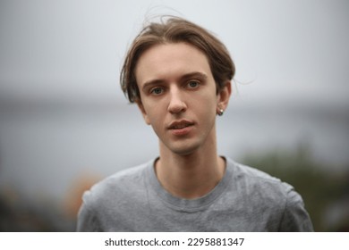 handsome young guy with ear piercing with long hair looking at camera and smiling seductively. autumn blurred background. close up portrait - Powered by Shutterstock