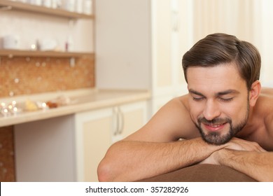 Handsome young guy is getting massage at spa. He is lying and smiling. His eyes are closed with relaxation. Copy space in left side
